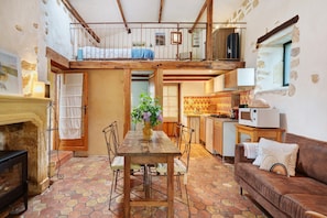 A rustic interior with a wooden dining table, a sofa, a kitchen area, and a loft bedroom with a bed.