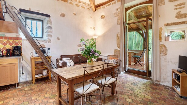 A rustic kitchen with a wooden table and chairs, a staircase, and a view through a glass door. - Charming Cottage in Biron (Biron)