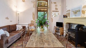 A rustic room with a stone wall, a wooden table, a brown leather sofa, a fireplace, and a large window. - Charming Cottage in Biron (Biron)