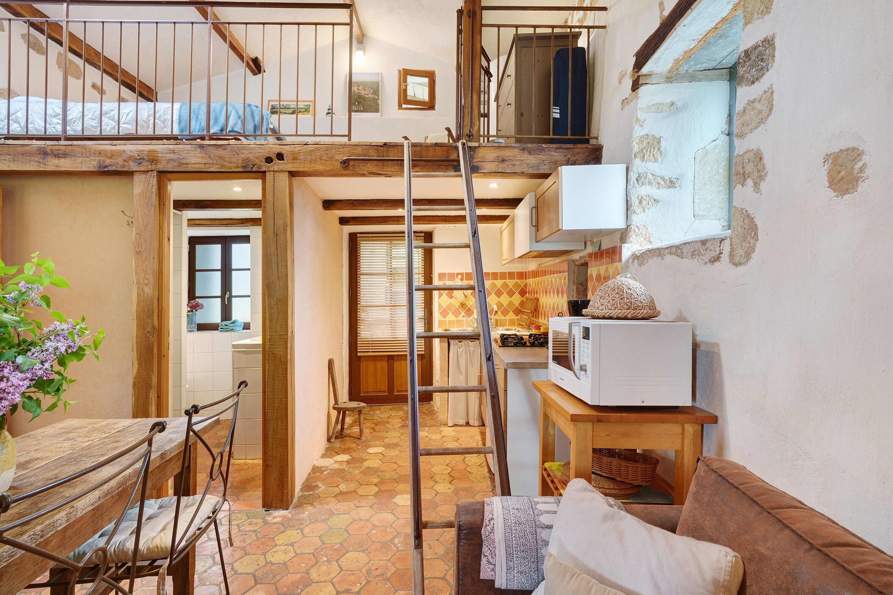 A compact kitchen with a wooden table, a ladder, and a microwave.