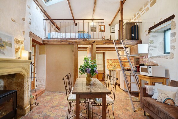 A rustic interior with a wooden dining table, chairs, a sofa, a fireplace, a staircase, and a loft bedroom.