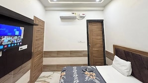 A hotel room with a bed, a TV mounted on the wall, an air conditioning unit, and a ceiling fan. - Devi Heritage (Mathura)