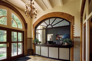 A reception area with a wooden reception desk, large arched windows, and a chandelier. - Landgoed Ehzerwold (Almen)