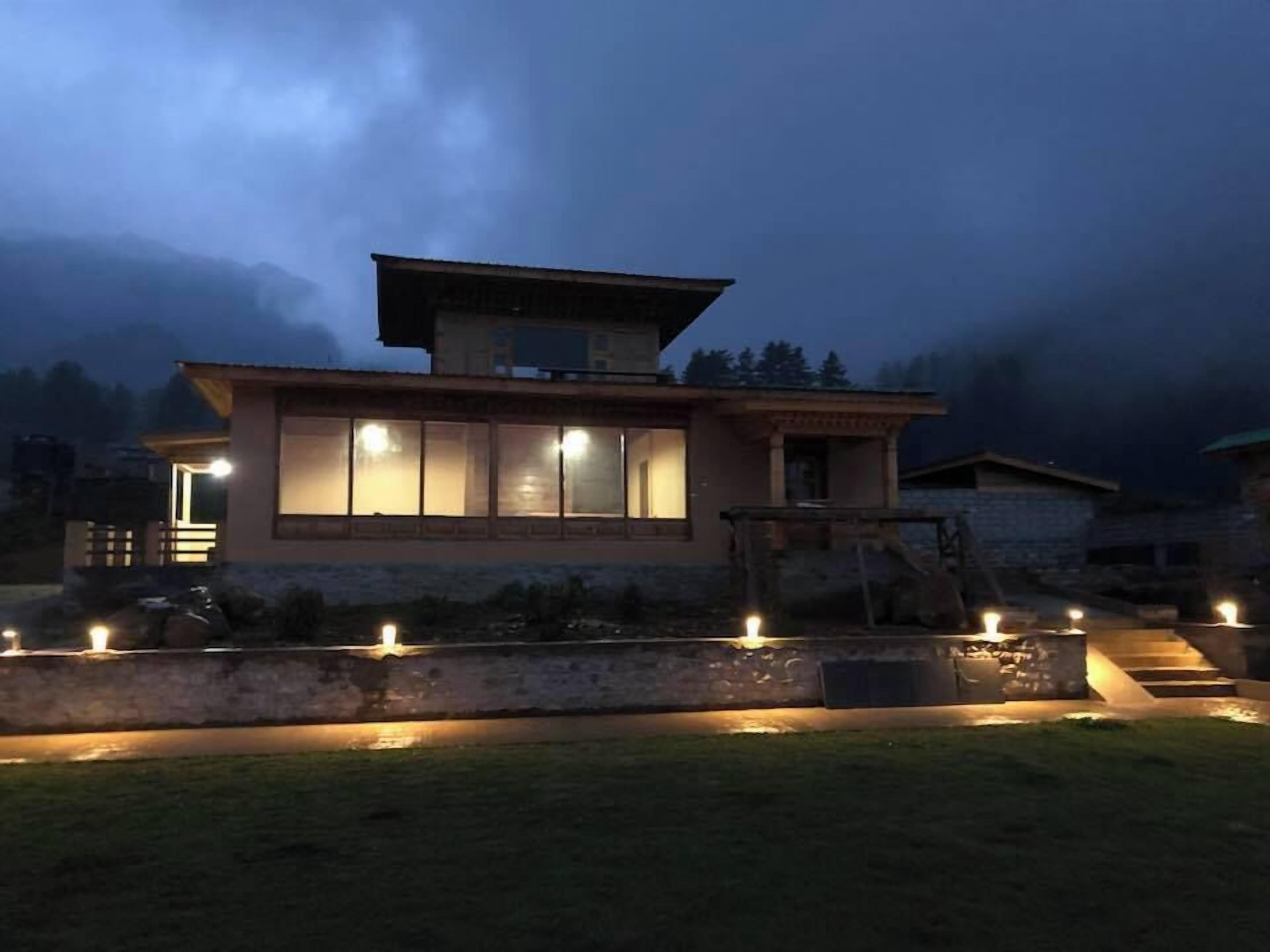 Une maison moderne dotée de grandes fenêtres et d’un toit plat, entourée d’un jardin bien éclairé.