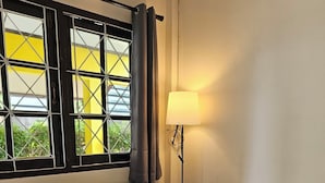 Quarto com sofá, mesa com um vaso de flores, luminária e janela com cortinas.