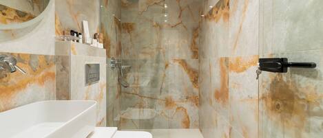 A modern bathroom with a large white sink, a glass shower enclosure, and marble walls.