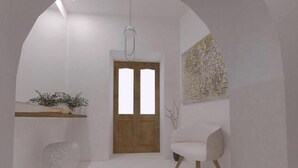 Un interior minimalista con una puerta de madera, una silla blanca, una pequeña mesa con una planta y una obra de arte abstracta colgada en la pared.