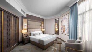 Ein Hotelzimmer mit einem großen Bett, Nachttischen, einem Sessel und einem großen Fenster mit Vorhängen.