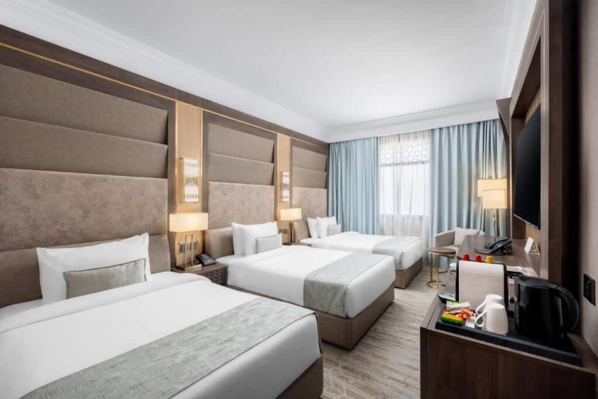 Ein Hotelzimmer mit drei Betten, einem Schreibtisch mit Kaffeemaschine und einem Fernseher.