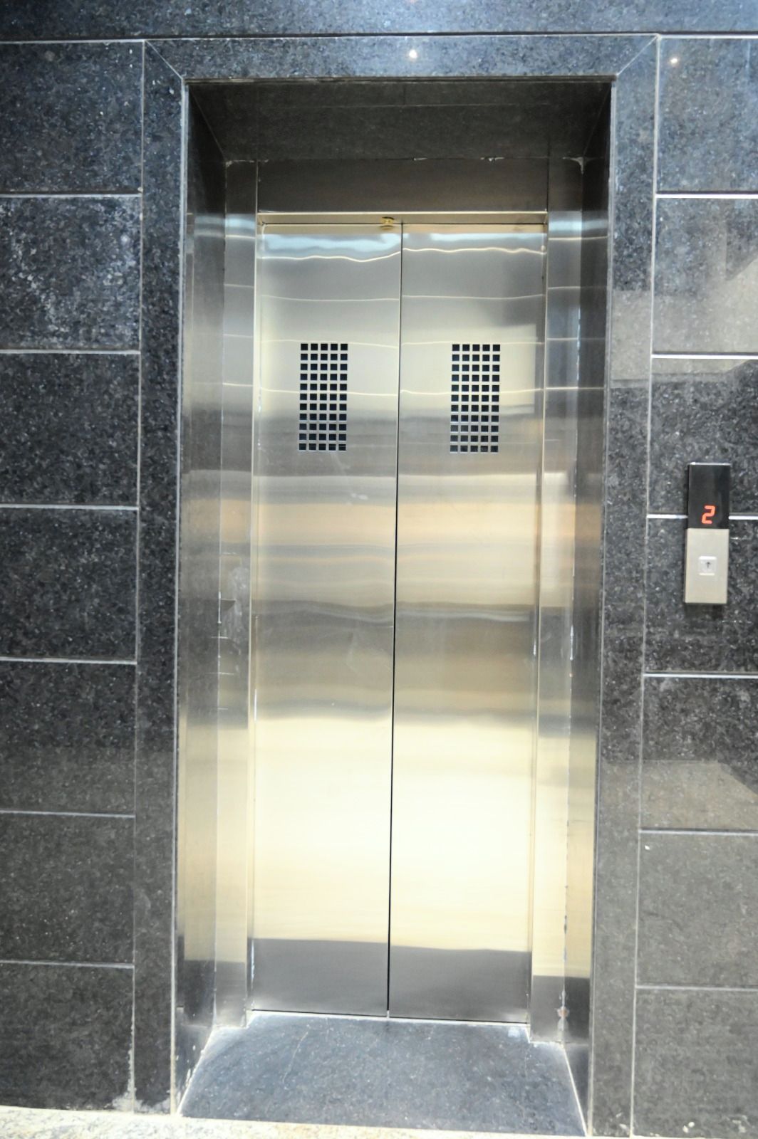 An elevator with a metallic finish, two ventilation grilles, and a digital display showing the number 2.