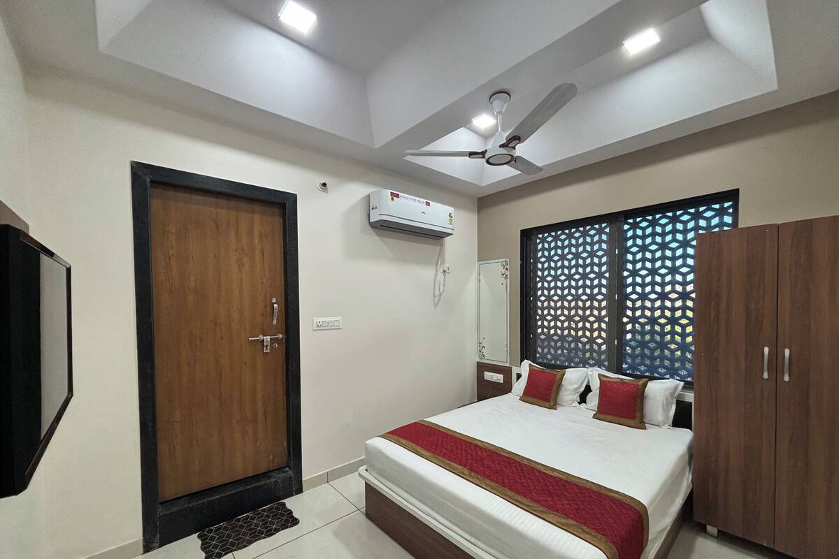 A bedroom with a bed, wardrobe, ceiling fan, air conditioning unit, and a decorative window screen.