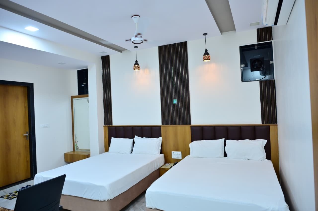 A hotel room with two beds, a ceiling fan, pendant lights, a mirror, and a small table.