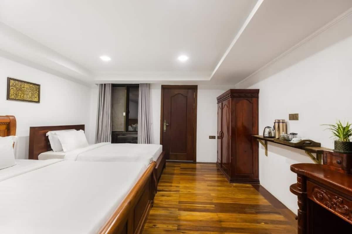 A hotel room with a large bed, wooden wardrobe, and a small shelf with items.