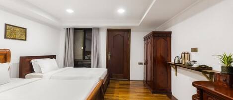 A hotel room with a large bed, wooden wardrobe, and a small shelf with items.