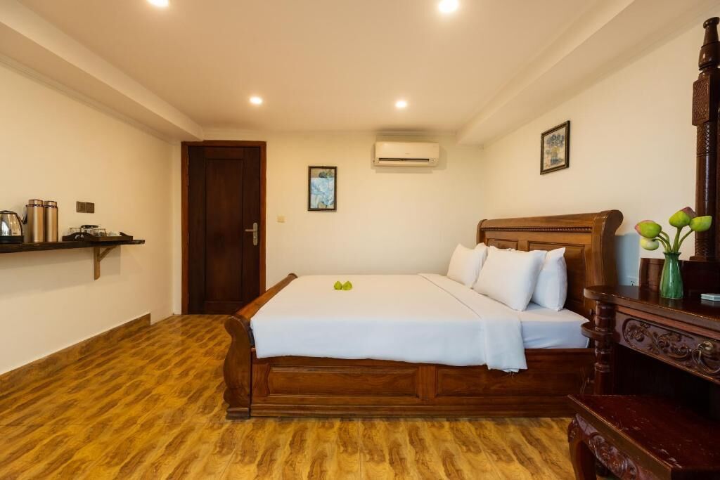 Een slaapkamer met een houten bed, nachtkastje, een plank met spullen, en een airconditioning.