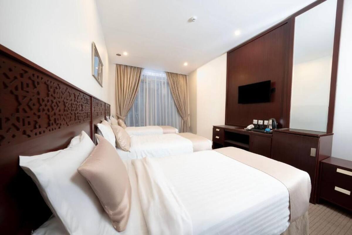 A hotel room with two beds, a TV, a desk, and a mirror.