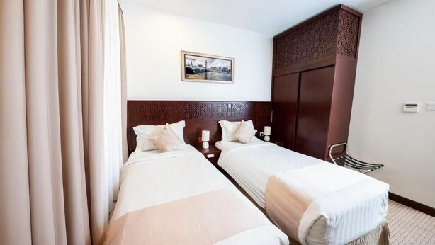Habitación de hotel con dos camas individuales, cabecera de madera, un armario grande y un cuadro en la pared.