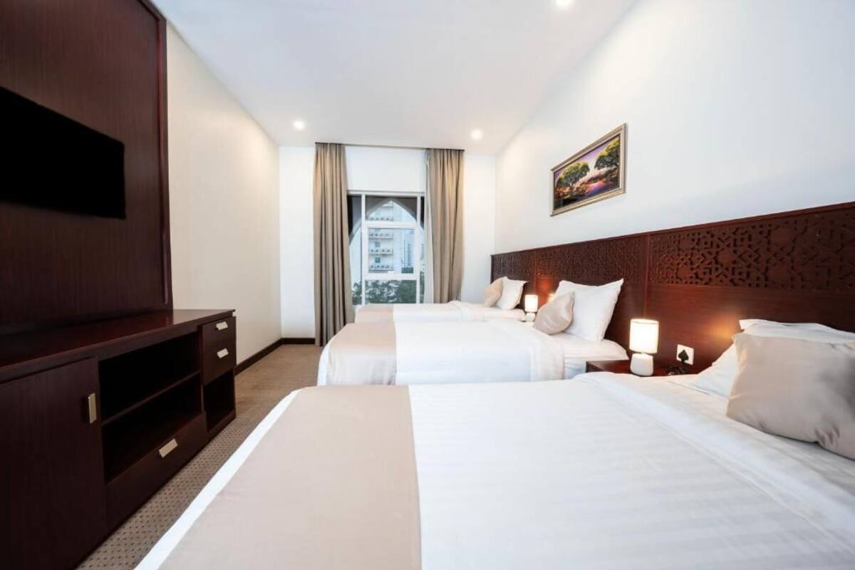 A hotel room with two beds, a TV, and a view of a building through the window.