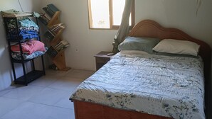 Quarto com cama de madeira, mesa de cabeceira, estante e janela com cortinas.