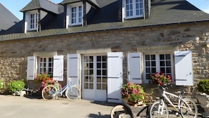 A stone building with a gabled roof, white shutters, and a bicycle parked in front. - Seaside Escape in Audierne: Maritime-Themed Cottage at the Tip of Southern Finistère (Audierne)