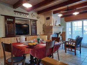 Un coin repas avec une nappe rouge, des chaises en bois, un téléviseur et une fenêtre donnant sur un beau paysage.