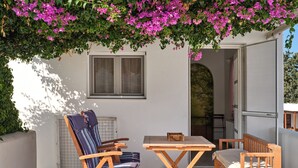 A patio with a wooden table and chairs, a radiator, and a window. - La Belle Casa de Parikia (Paros)