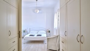 A bedroom with a bed, bedside tables, a chair, and a wardrobe. - La Belle Casa de Parikia (Paros)