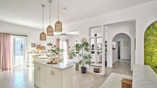 A spacious kitchen with a central island, pendant lighting, and a view of a lush garden through an archway. - La Belle Casa de Parikia (Paros)