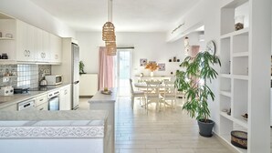 A modern kitchen with white cabinets, a central island, and a dining area with a table and chairs. - La Belle Casa de Parikia (Paros)