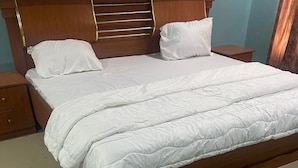 A neatly made bed with white bedding, a wooden headboard with horizontal slats, and a wooden nightstand on the left. - Room-flexible 8-bedroom Luxury Apartment (Benin City)