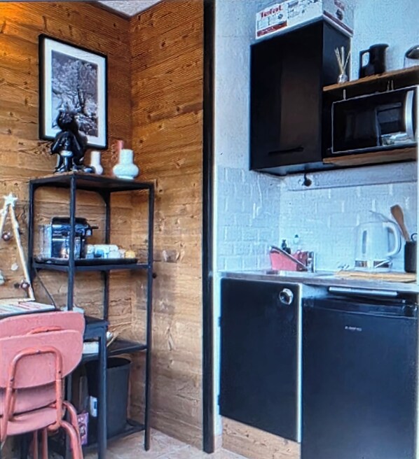 A compact kitchen with a wooden wall, a small shelf with kitchen items, a microwave, and a dishwasher.