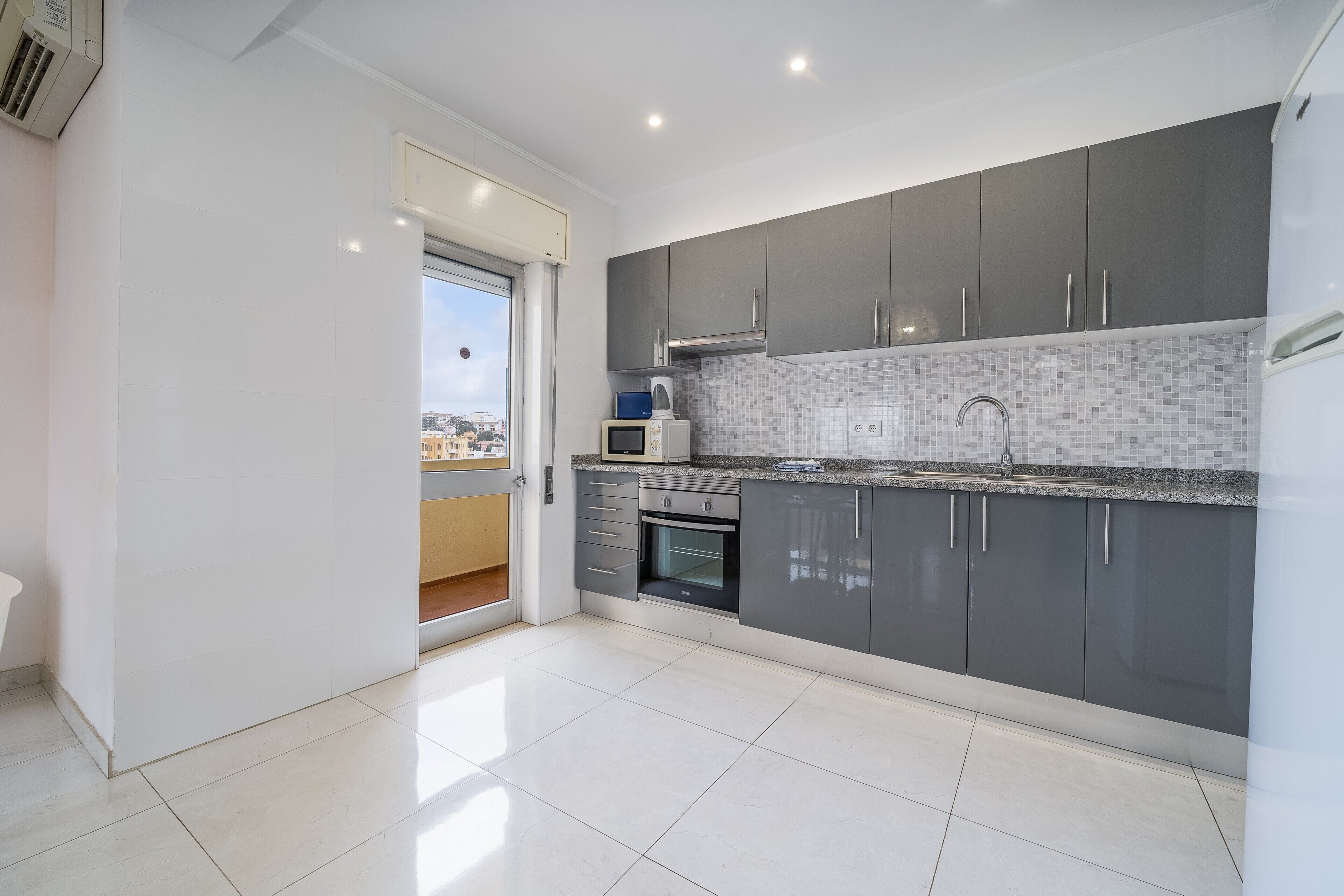 A modern kitchen with grey cabinets, a tiled backsplash, and a built-in oven.