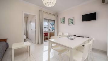 A dining area with a white table and chairs, a ceiling light fixture, and a flat-screen TV mounted on the wall.