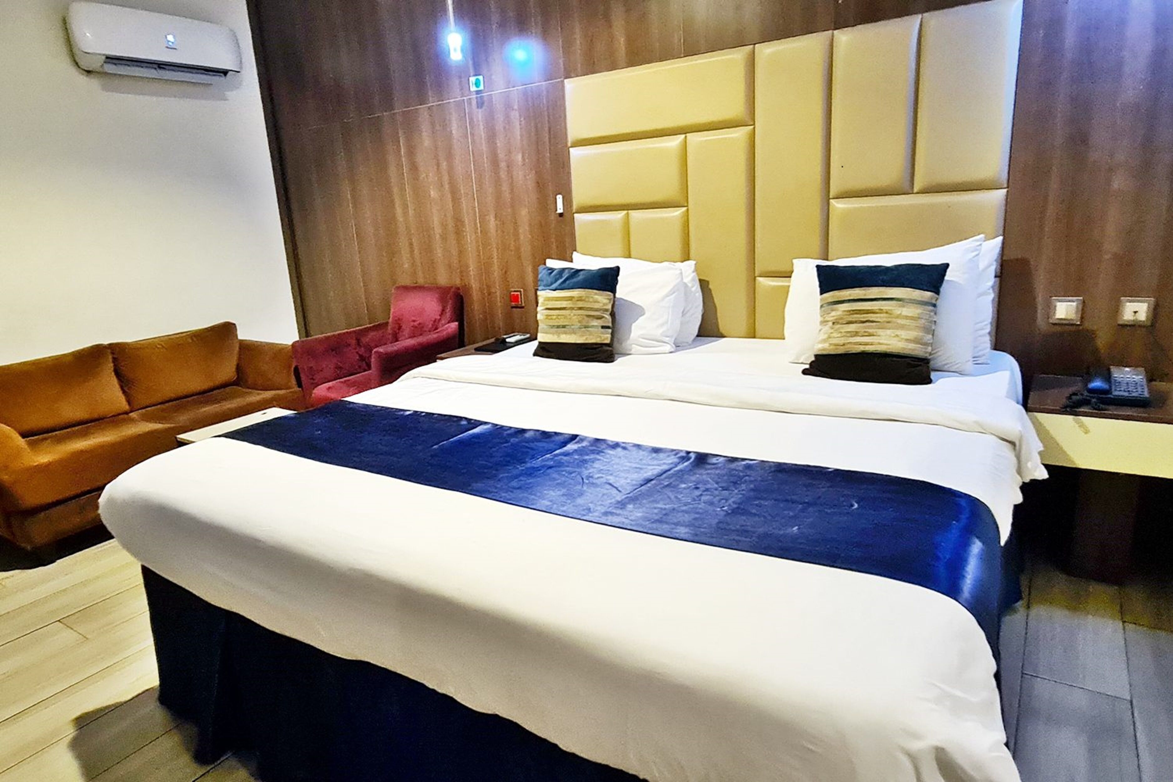 Una habitación de hotel con una cama grande, un sillón rojo y un cabecero de madera.