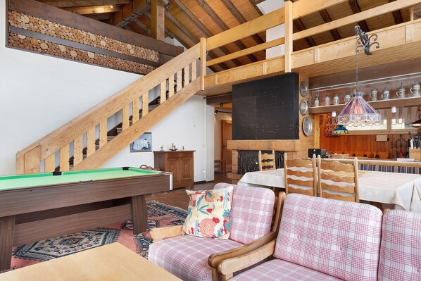 Un escalier en bois, une table de billard, un canapé et un coin repas avec des chaises et une table.