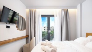 Ein Hotelzimmer mit Bett, Wandfernseher, Vorhängen am Fenster und Blick auf Gebäude.