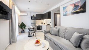 Ein modernes Wohnzimmer mit einem grauen Sofa, einem Esstisch mit Stühlen und einer Küche im Hintergrund.
