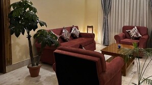 A living room with a red sofa set, a coffee table, and two potted plants. - Heritage Homestay  (Sivasagar)
