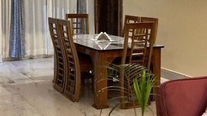 A dining area with a wooden table and chairs, a red couch, and a potted plant. - Heritage Homestay  (Sivasagar)