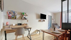 Ein modernes Wohnzimmer mit einem Holzesstisch, einem an der Wand montierten Fernseher und einem Bücherregal mit verschiedenen Gegenständen.