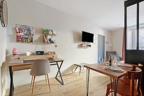 Un salon moderne avec une table à manger en bois, un téléviseur fixé au mur et une bibliothèque contenant divers objets.