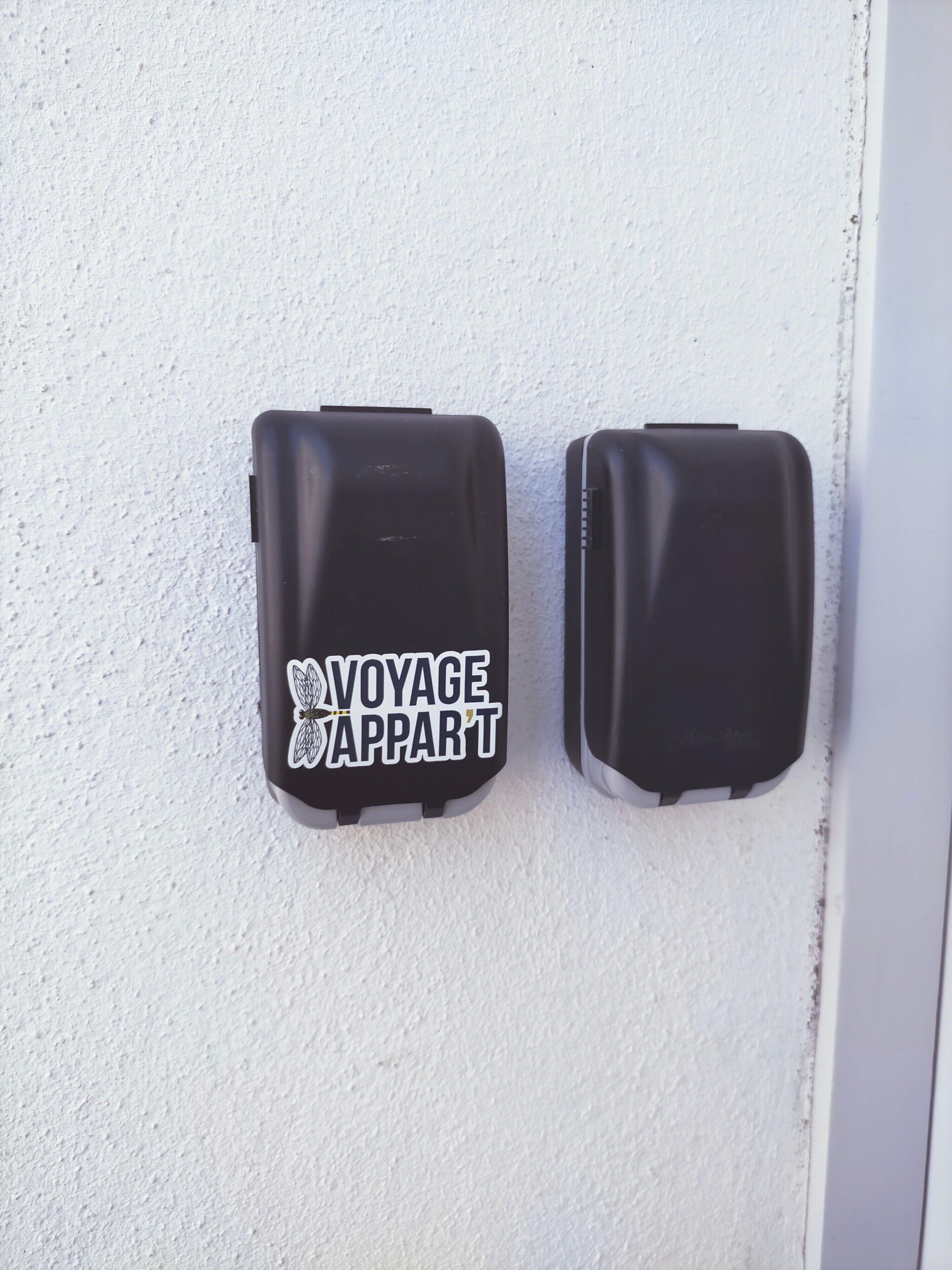 Twee zwarte objecten met een wit label op een ruwe witte muur.
