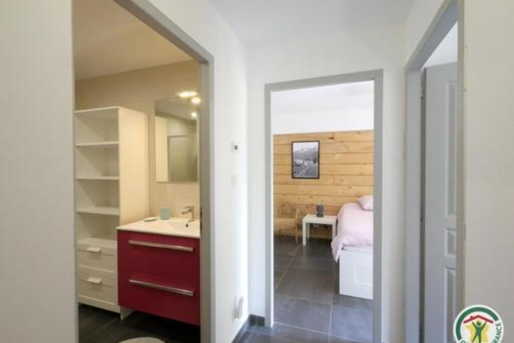 Een moderne badkamer met een rode wastafel, een witte wasbak en een spiegel. Er is een houten wand en een klein tafeltje met een handdoek.