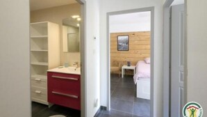 A modern bathroom with a red vanity, a white sink, and a mirror. There is a wooden wall and a small table with a towel. - Gîtes de la Lame - L'Écurie : Authentic charm and serenity in the heart of the Écrins mountains (Réallon)