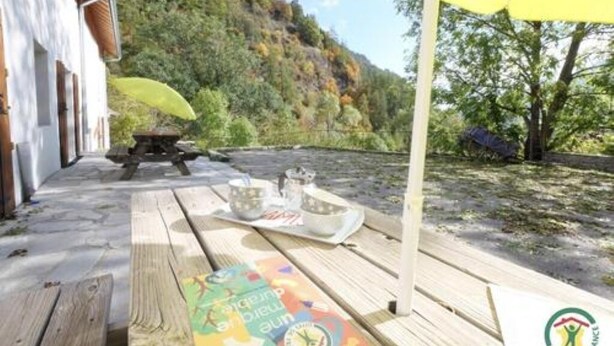 An outdoor wooden deck with a picnic setup, including a table, chairs, and a yellow umbrella. - Gîtes de la Lame - L'Écurie : Authentic charm and serenity in the heart of the Écrins mountains (Réallon)