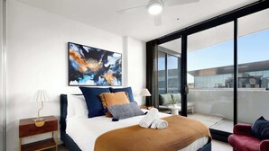 Ett modernt hotellrum med en stor säng, utsikt över staden genom fönster som sträcker sig från golv till tak, en balkong och ett samtida konstverk på väggen.