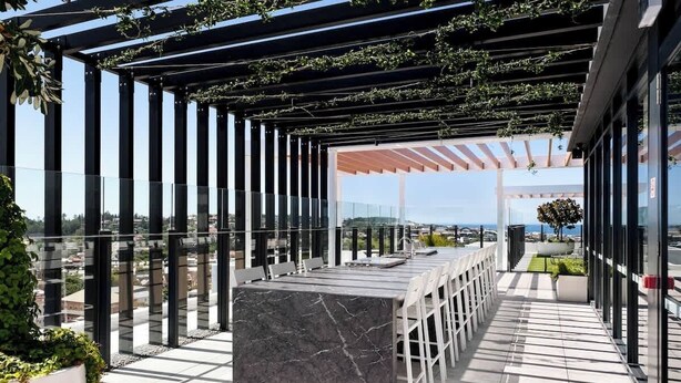 En utomhusterrass med en bardisk i marmor, sittplatser och en pergola som är täckt med grönska.