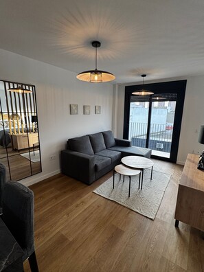 A modern living room with a dark grey sofa, a round coffee table, and a large window with a view of buildings.