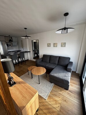 A modern living room with a grey sectional sofa, a wooden coffee table, and a dining area with a kitchen in the background.