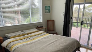Une chambre à coucher comprenant un lit, deux tables de chevet, une chaise, une fenêtre avec des stores et une vue sur l’extérieur.
